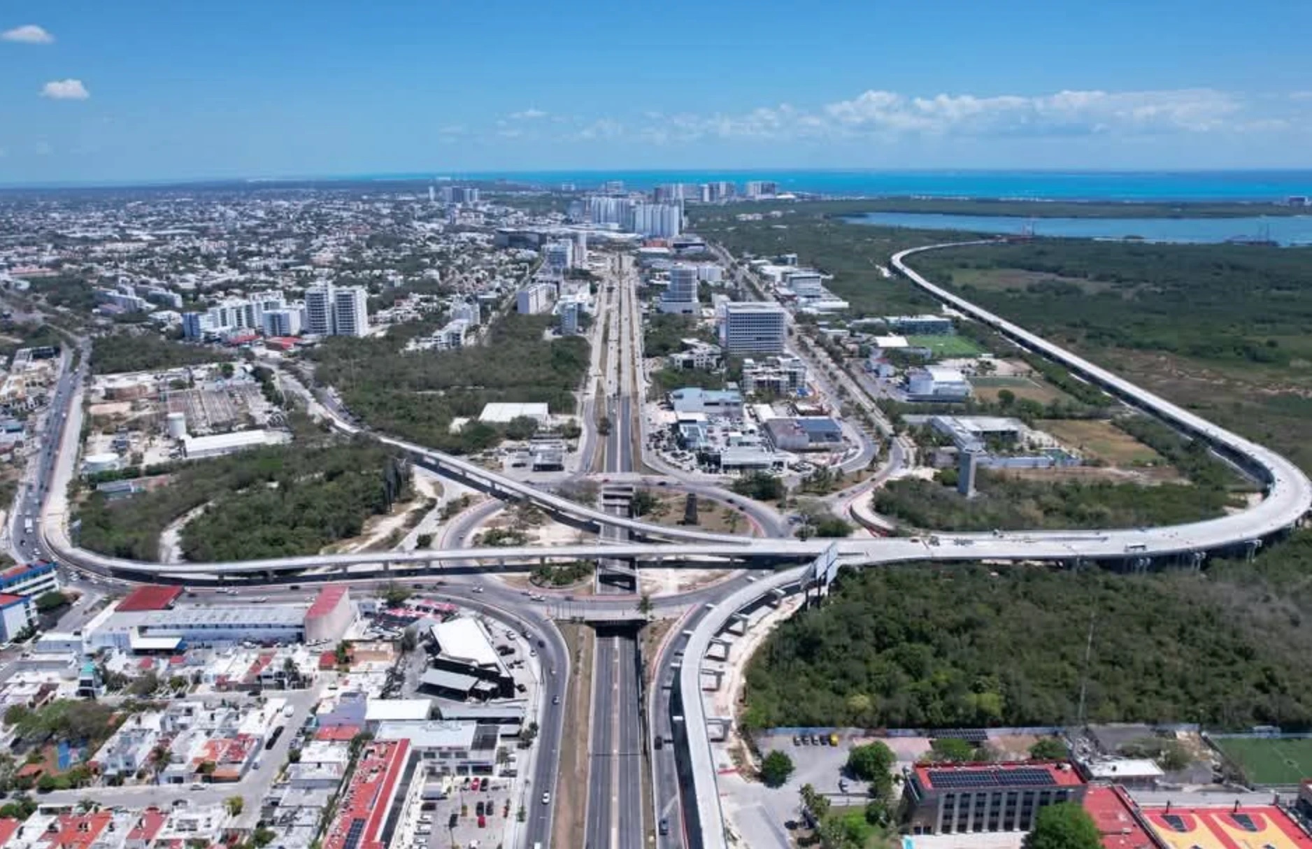 Vista aérea del entronque del Blvd. Colosio con la Av. Kabah y el viaducto del puente Nichupté: los distribuidores viales, la ciudad al fondo y el Caribe en el horizonte.