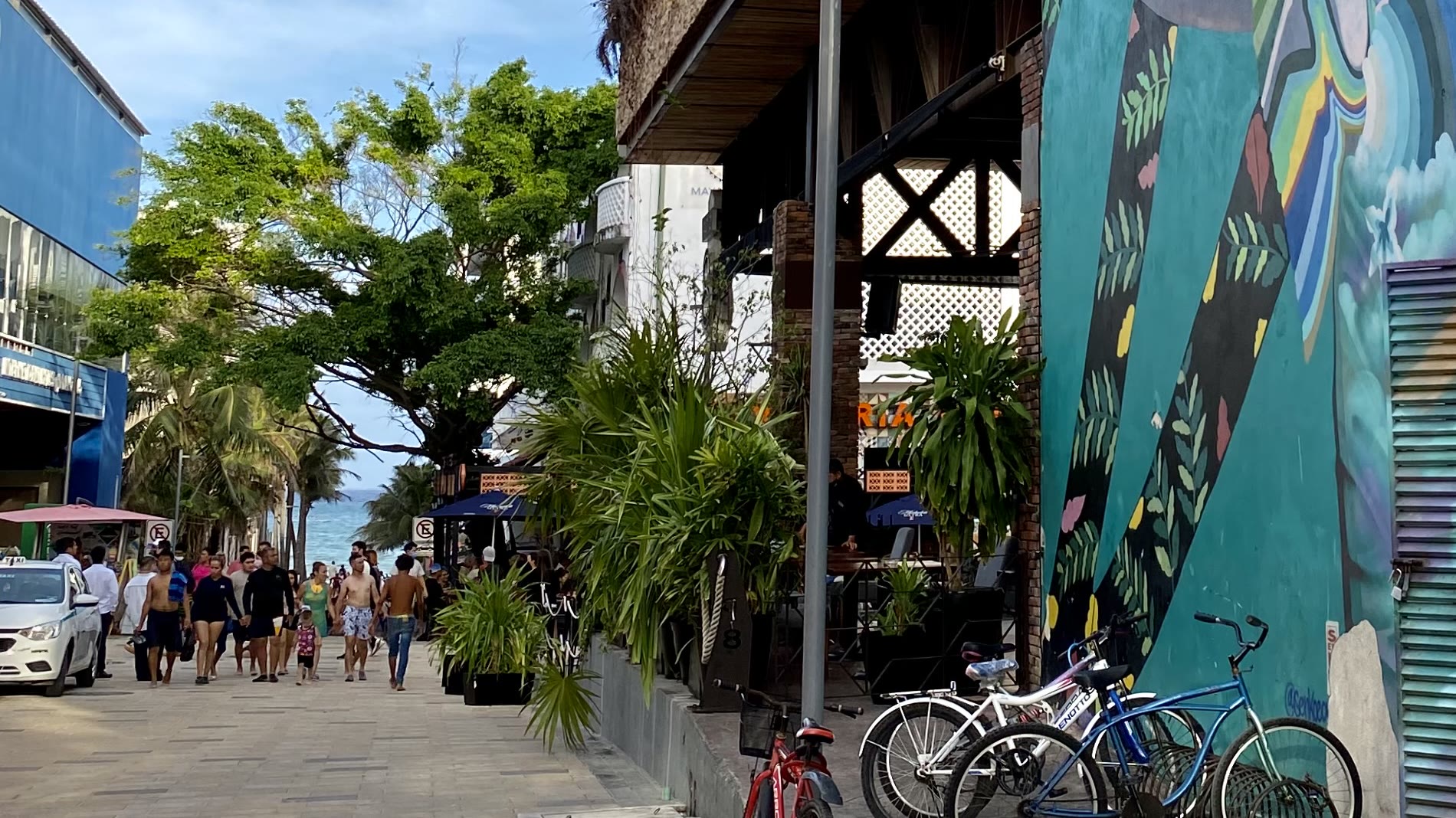La Quinta Avenida de Playa del Carmen: calle peatonal con gente caminando, bicicletas y el mar al fondo.