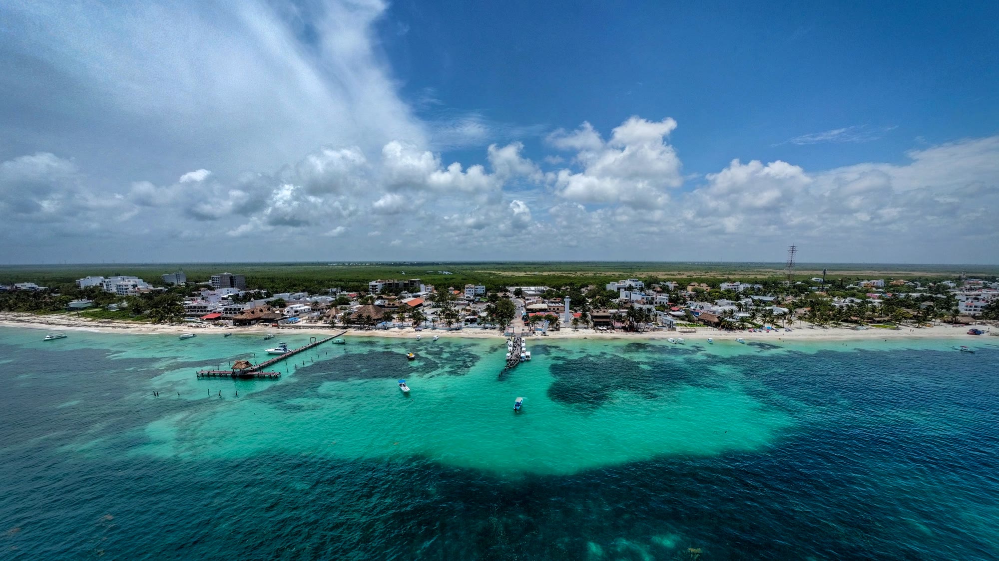Puerto Morelos desde el aire: el pueblo bajo junto a la playa, los muelles, el faro y el arrecife bajo el agua.